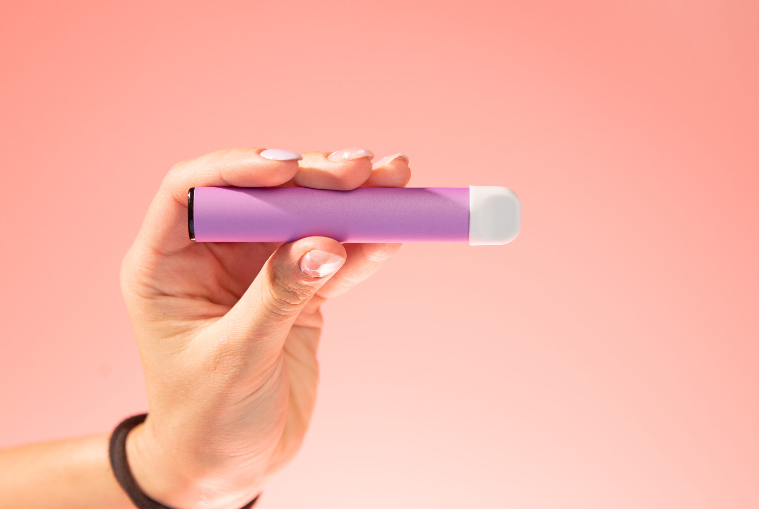 Hand holding pink vape pen on salmon-colored background 